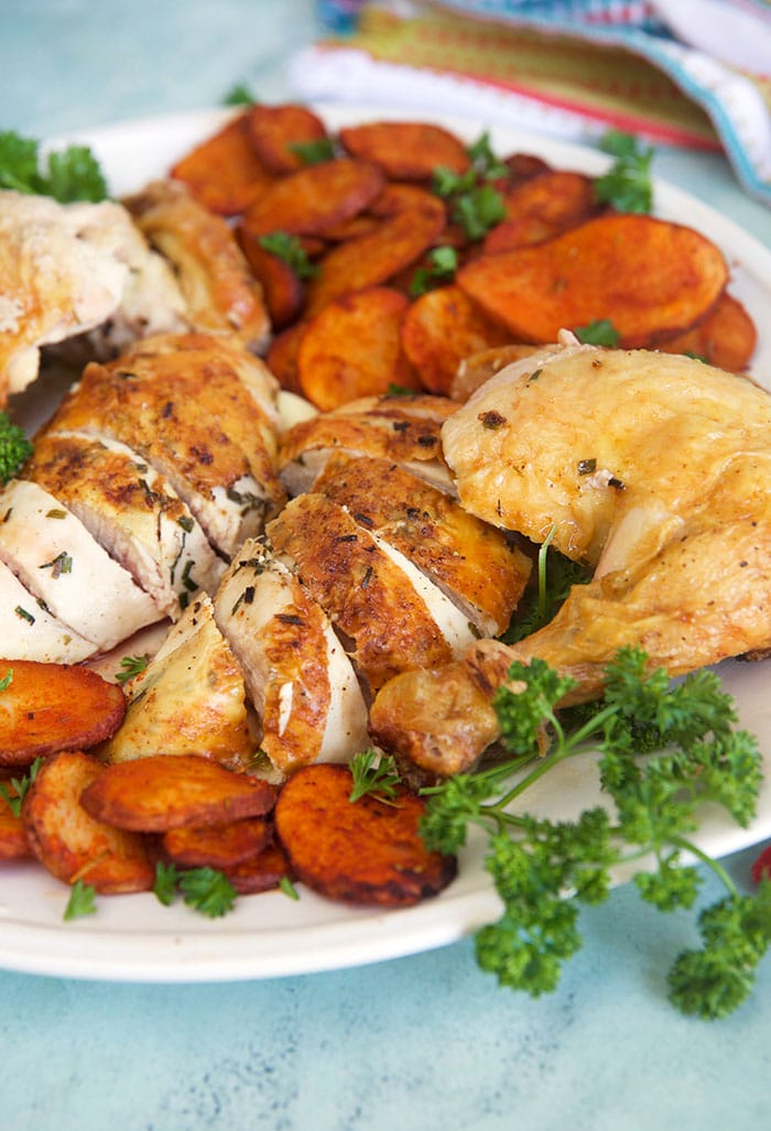 Oven roasted chicken on a white platter with potatoes.