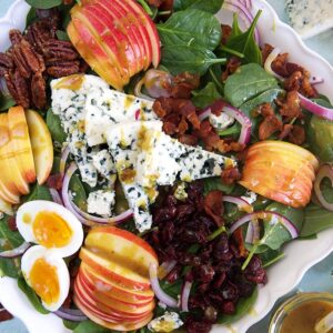 A spinach salad is loaded with ingredients like nuts, hard boiled eggs and apple slices.