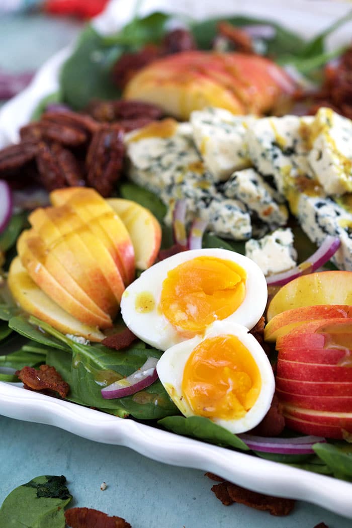 Hard boiled eggs, cheese, apples and spinach are all in one large white serving tray. 