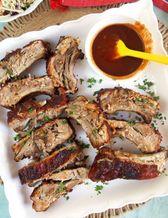 BBQ Pork ribs on a white platter with a bowl of sauce.
