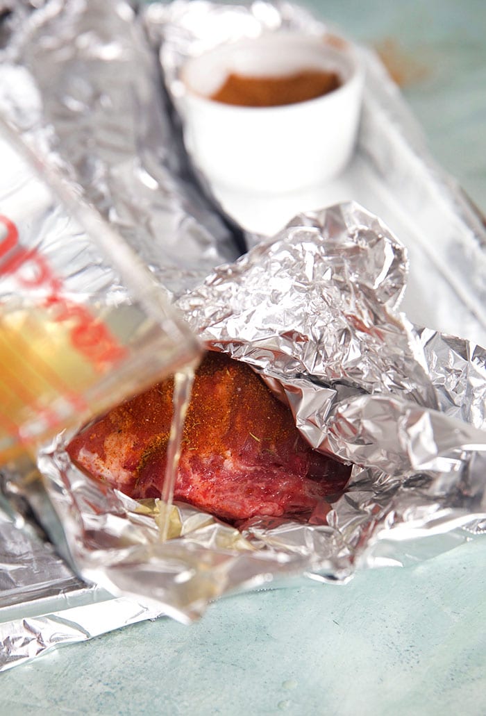 braising liquid being poured into a foil packet with ribs.