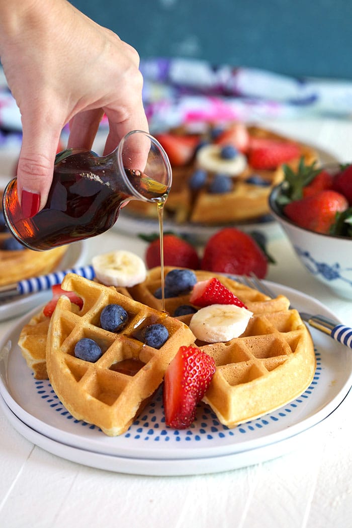 Belgian Waffle with fruit and syrup being poured over top.