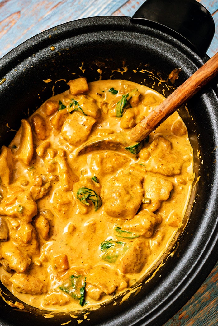 Overhead shot of butter chicken in a slow cooker with a wooden spoon.