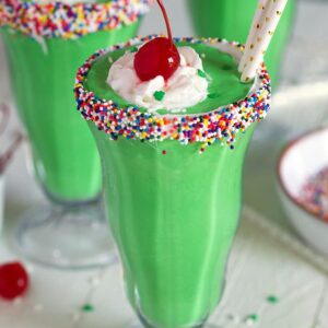 Shamrock shake in a milkshake glass with whipped cream and a cherry.