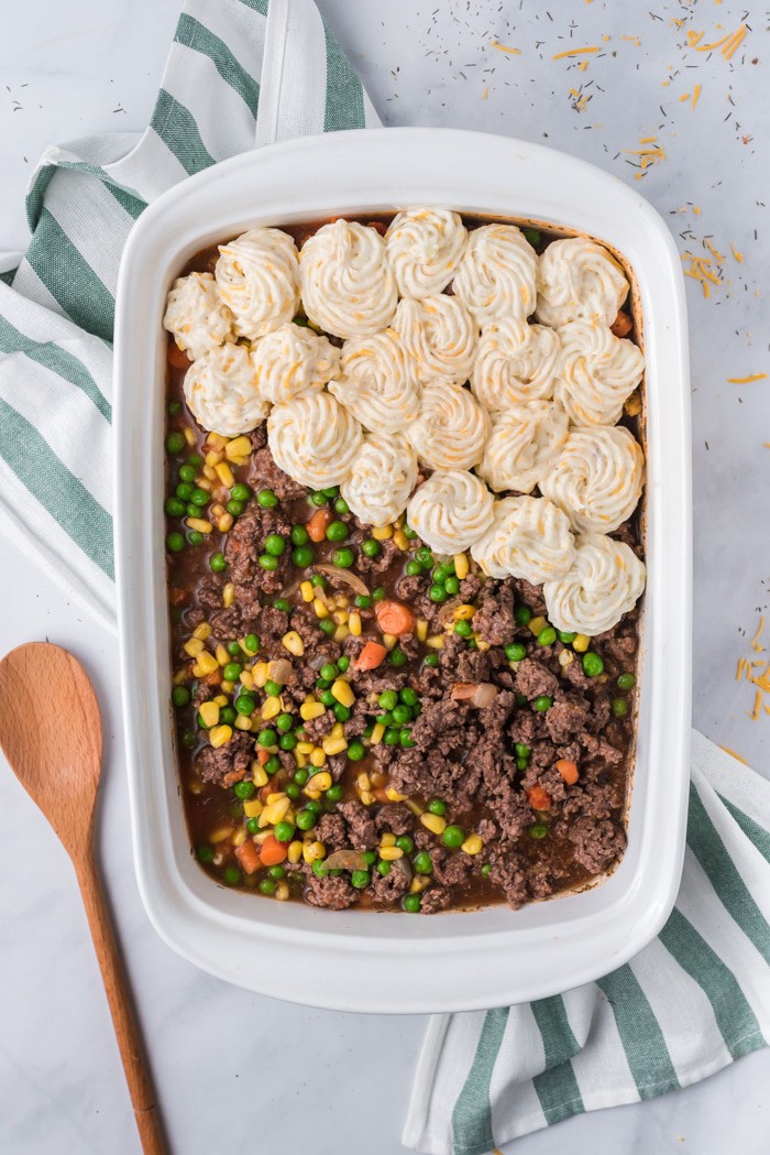 Shepherd's Pie in a casserole dish with mashed potatoes being piped on top.