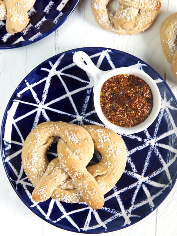 overhead shot of a sourdough pretzel on a blue plate with a white dish of mustard.