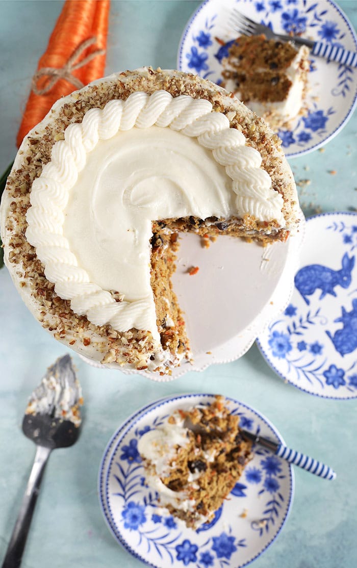overhead shot of carrot cake on a cake plate with a slice on a blue and white plate.
