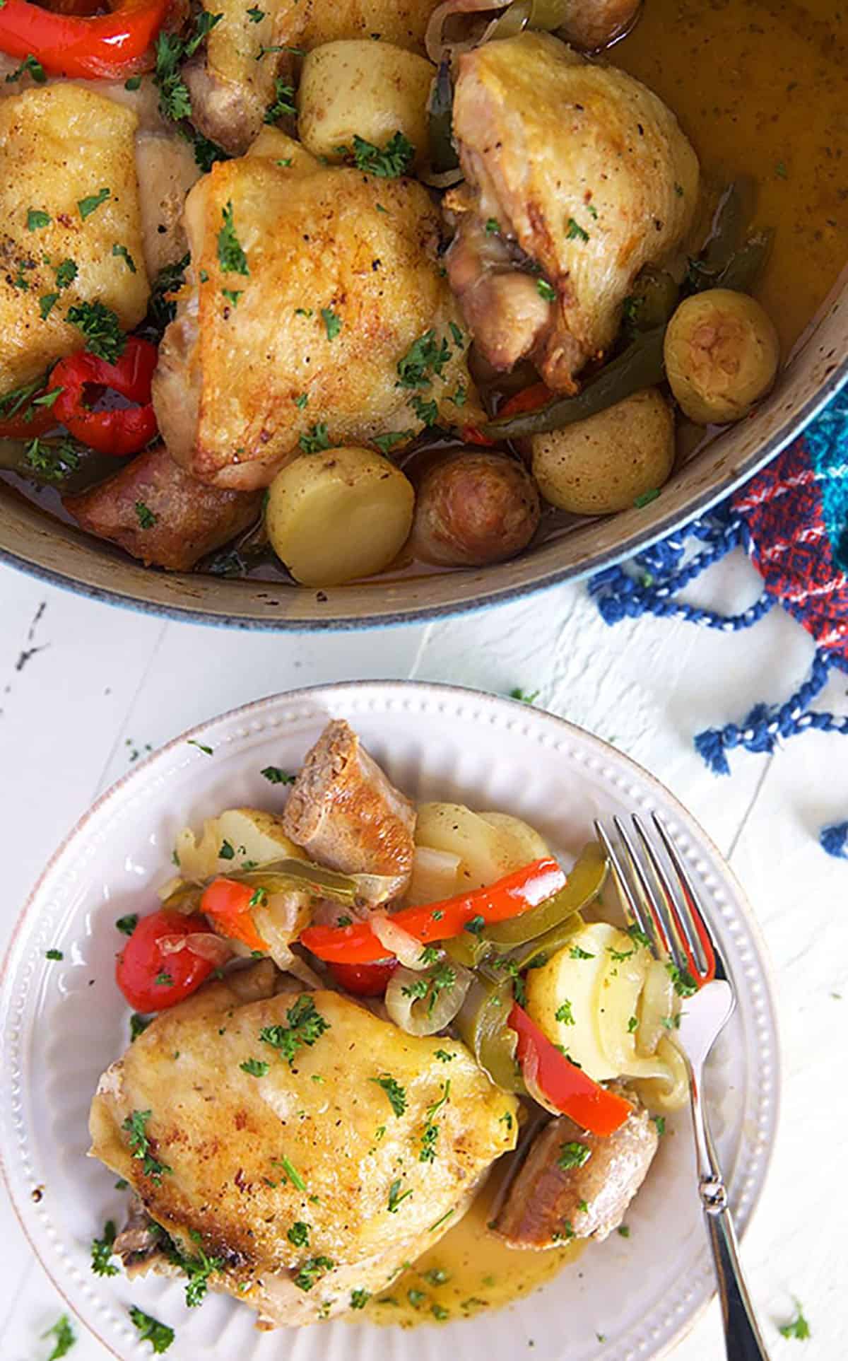 Chicken scarpariello on a white plate with a fork and a pot of chicken.