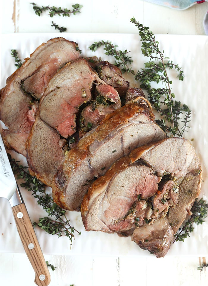 Sliced leg of lamb roast on a white platter.