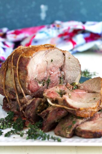 Roast Leg of Lamb stuffed with herbs on a white platter.