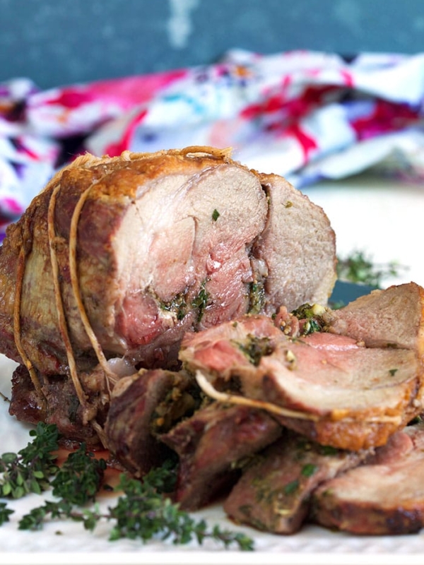 Roast Leg of Lamb stuffed with herbs on a white platter.