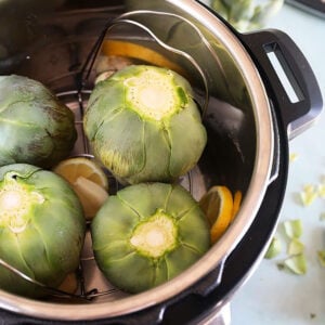 Trimmed artichokes in an Instant Pot on a blue background.
