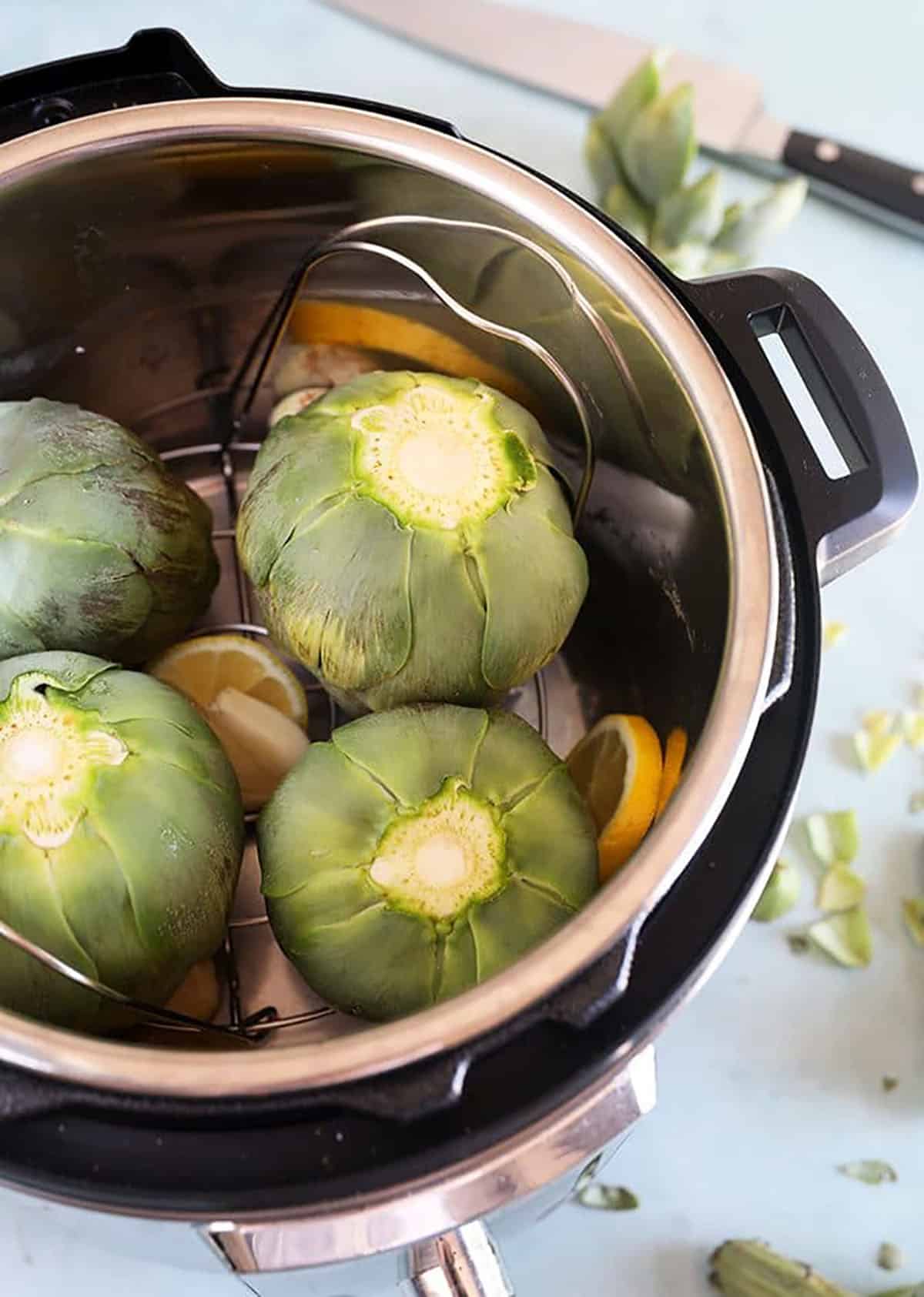 Trimmed artichokes in an Instant Pot on a blue background.