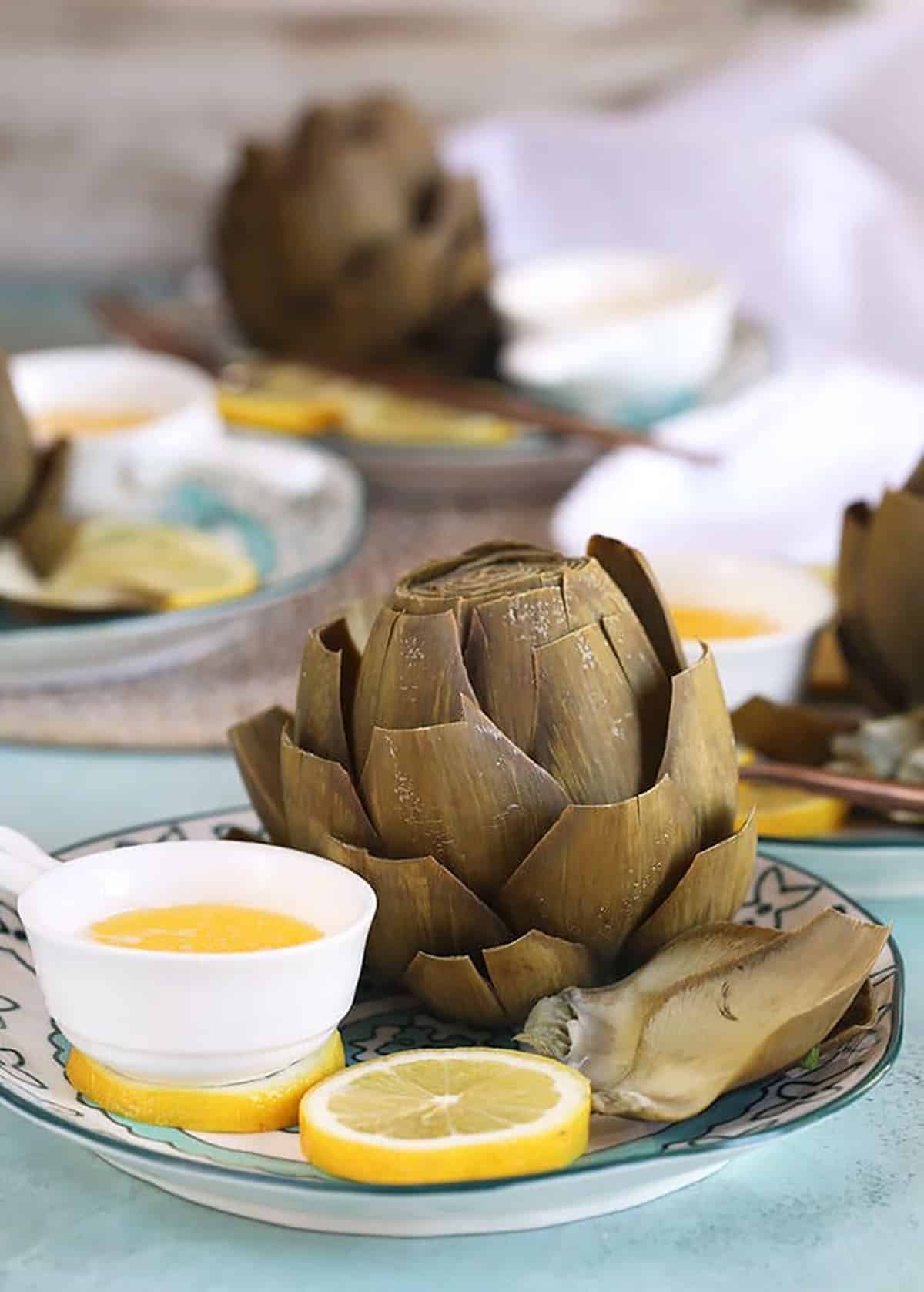 Instant Pot artichokes on a plate with lemon slices and melted butter.