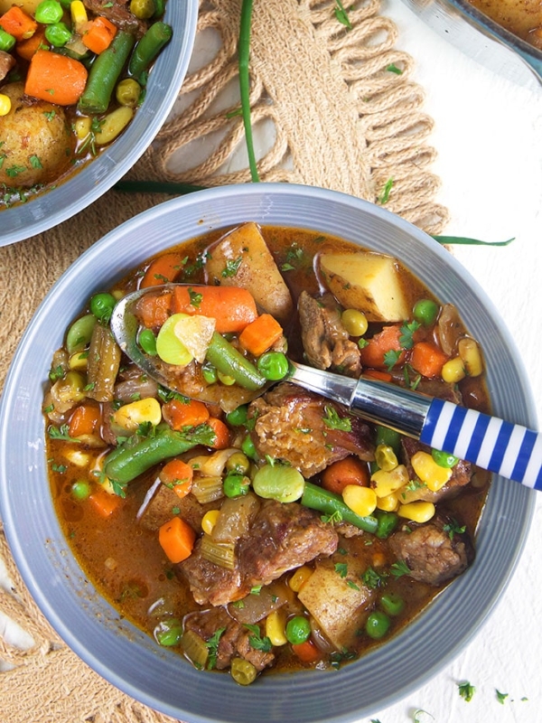 Overhead shot of mulligan stew in a gray bowl with a blue and white spoon in the bowl.