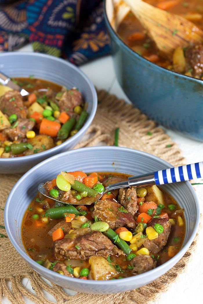 Beef Stew in a gray bowl with a blue and white striped spoon.