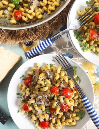 Overhead shot of pesto cavatappi pasta in a white bowl with a blue and white striped fork.