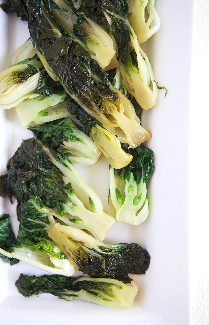 Cooked Bok Choy is dark green in color, presented on a white plate.