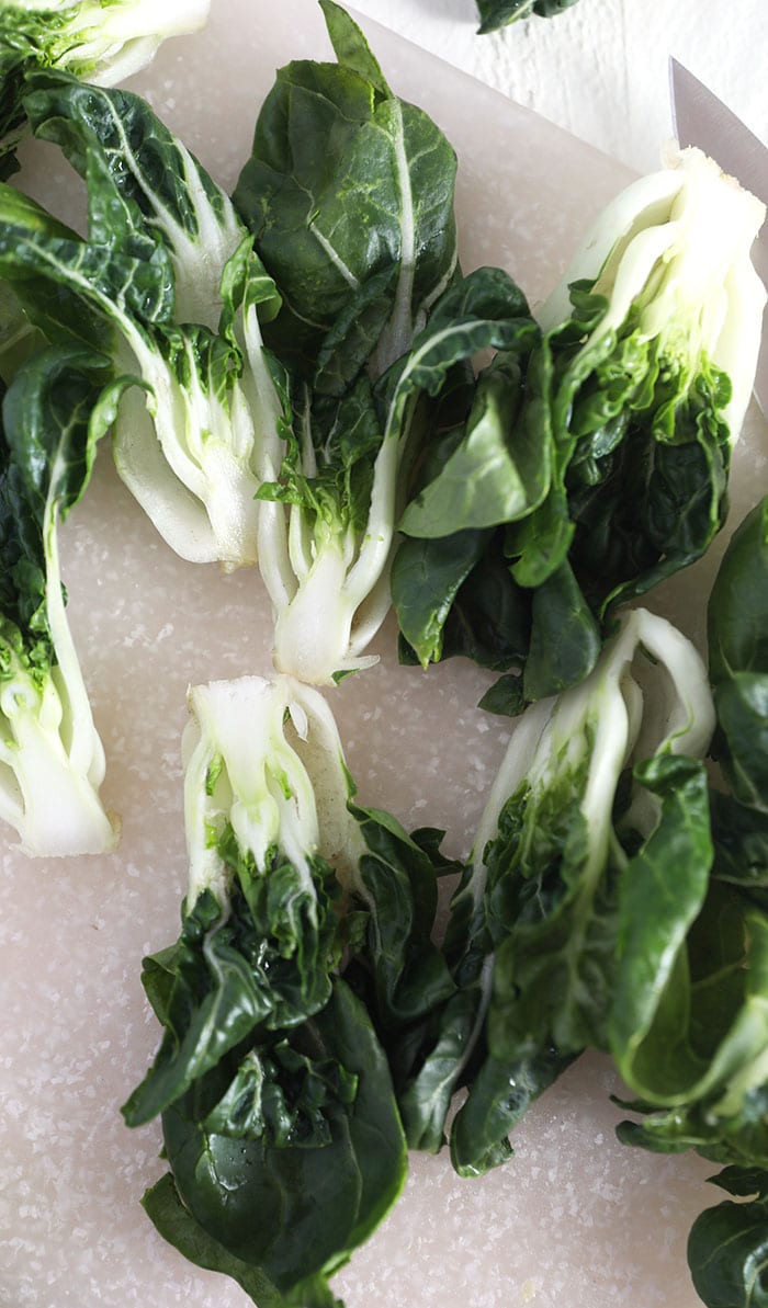 Bok choy is uncooked on a white surface.