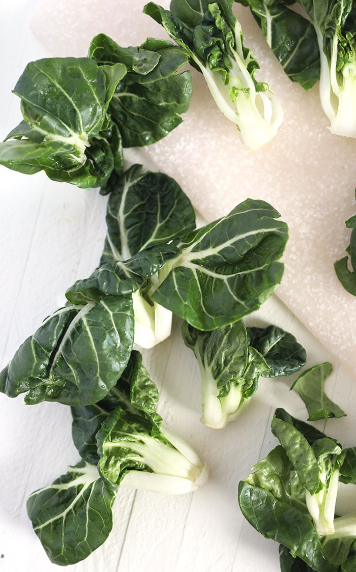 Pieces of dark green Bok Choy are placed on a white counter.
