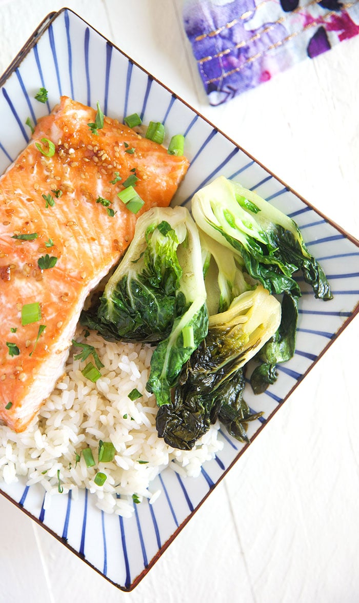 A piece of cooked salmon is presented on a plate, next to bok choy and white rice.