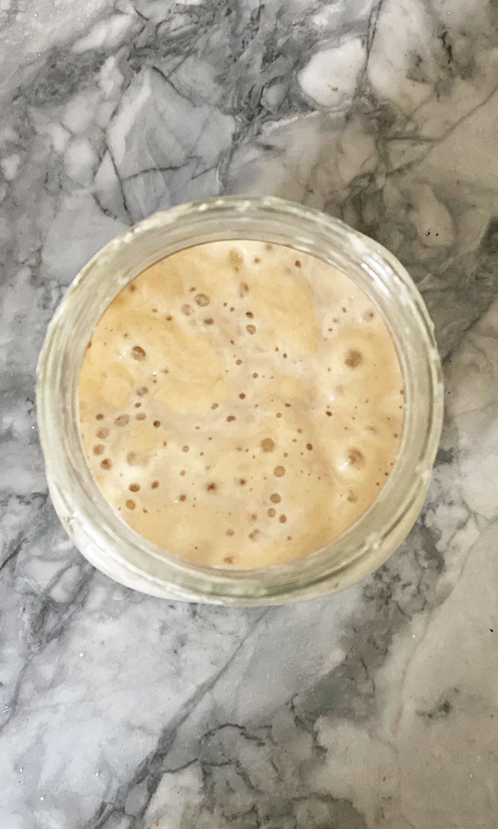 Sourdough starter with bubbles on a marble countertop.
