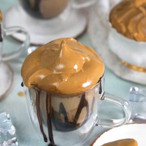 Whipped Coffee Mudslide on a blue background with a gold spoon on a white plate.