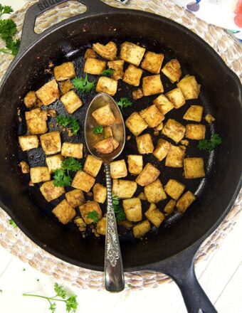 Crispy baked tofu is in a black skillet with a spoon.