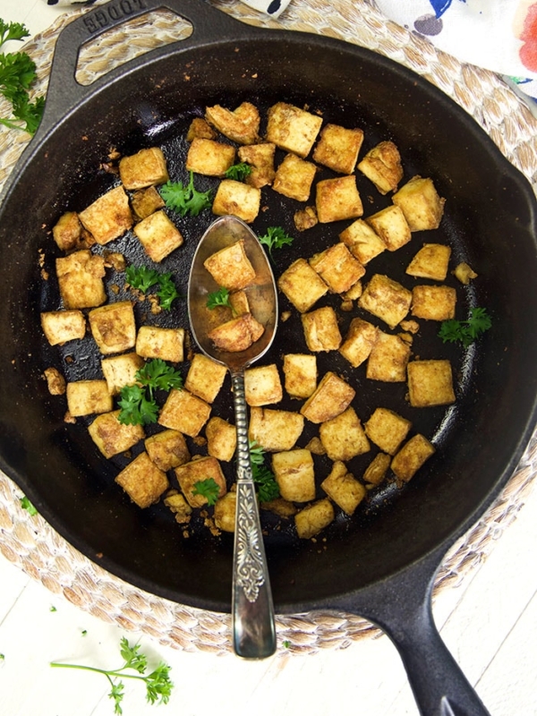 Crispy baked tofu is in a black skillet with a spoon.