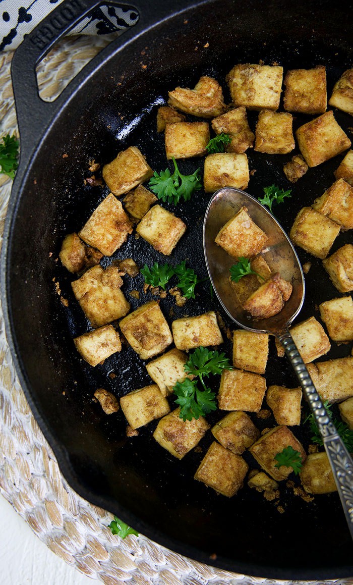 A spoon is placed in a large black skillet filled with tofu.