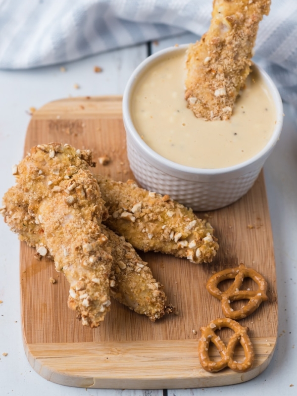 Overhead shot of pretzel crusted chicken tenders on a board with dipping sauce.