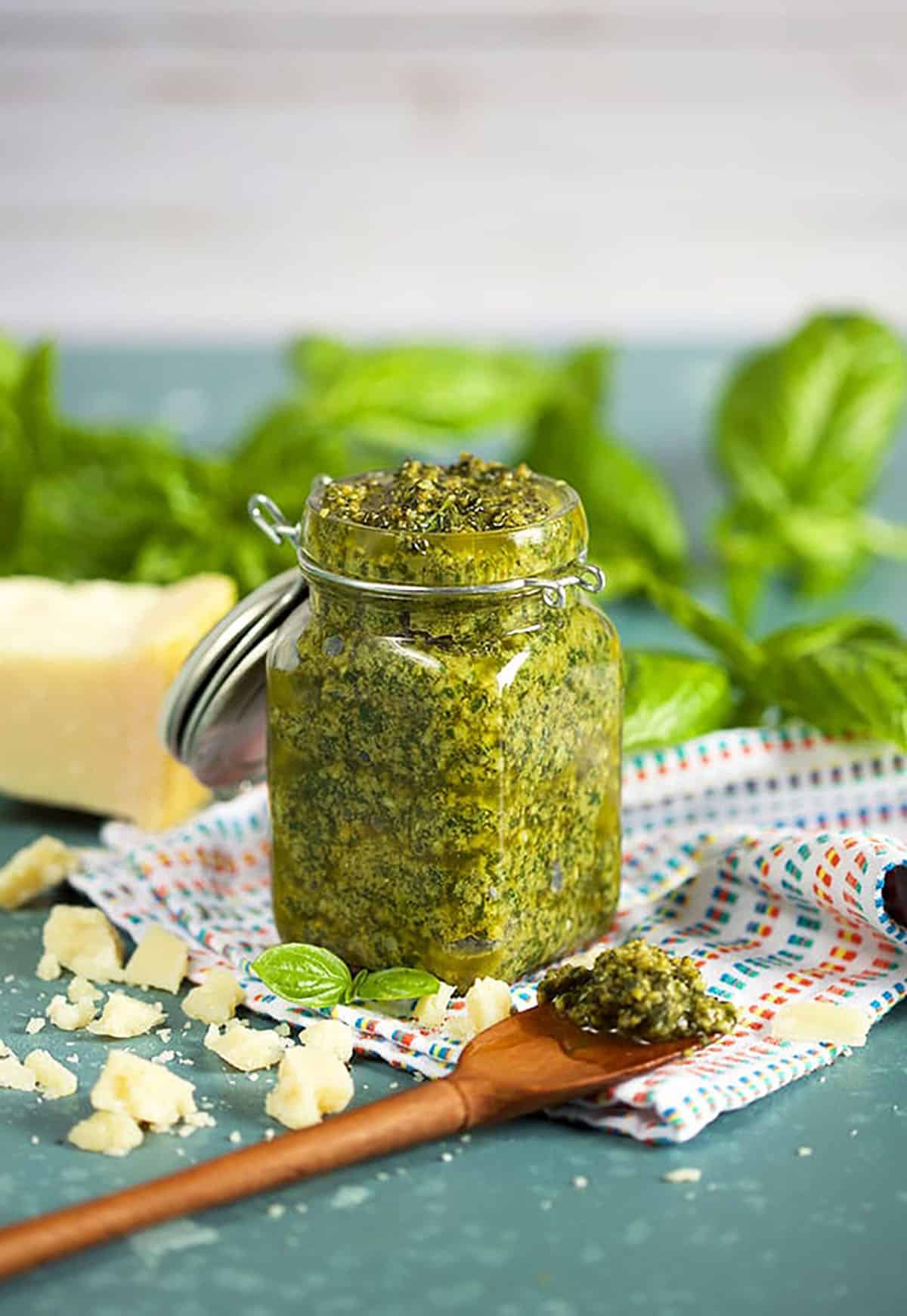 Basil Pesto in a small jar with a wooden spoon on the table.
