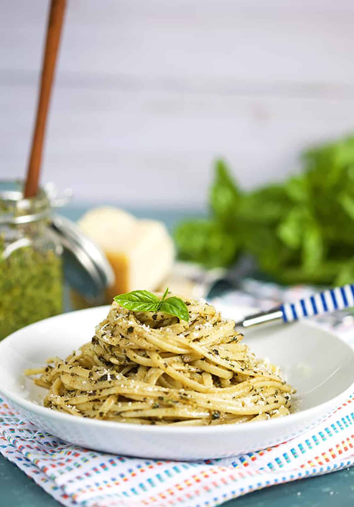 Pasta with Basil Pesto Sauce in a white bowl with a jar of basil pesto in the background