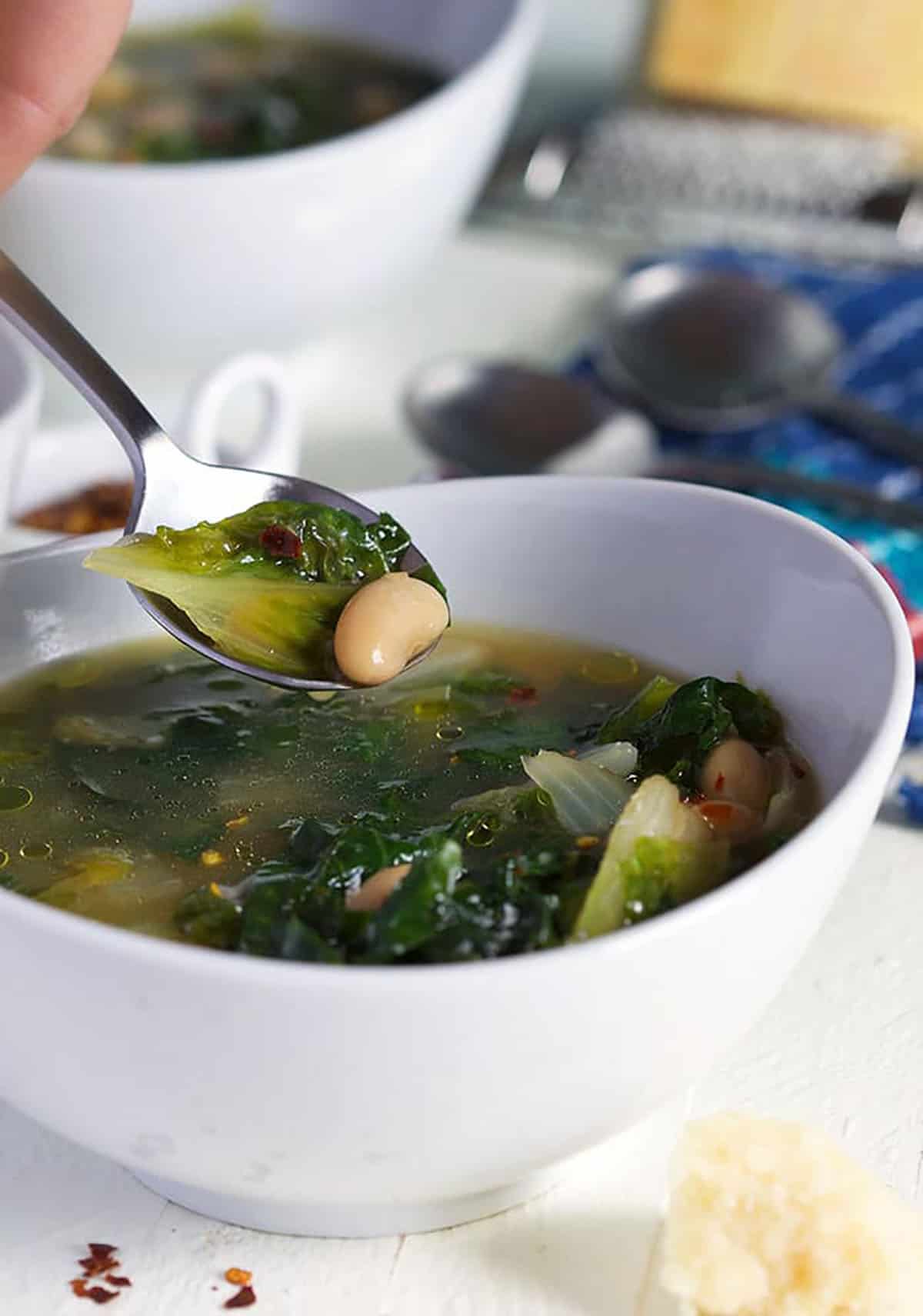 Escarole soup on a silver spoon over a bowl of soup in a white bowl.