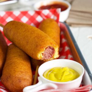 Corn dog with a bite out of it and a dish of mustard.