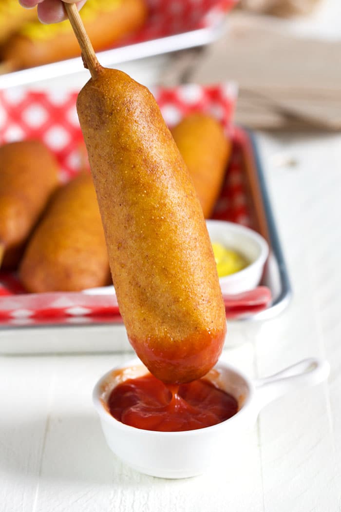 Corn dog being dipped into ketchup.