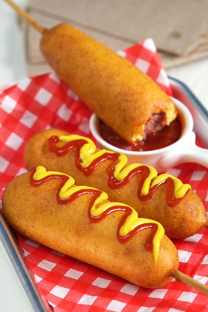 Corn dogs on a red and white paper.