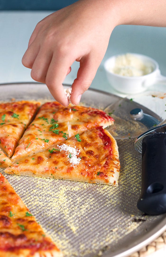 Childs hand sprinkling cheese on a thin crust pizza.