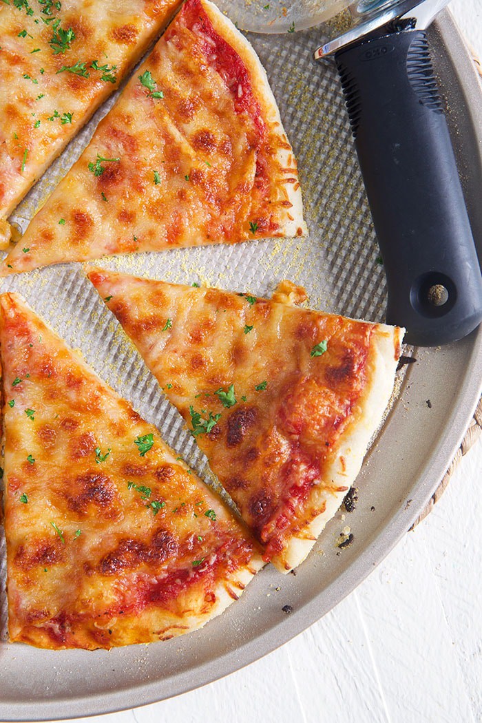 Thin Crust Pizza on a pizza pan with a pizza cutter.