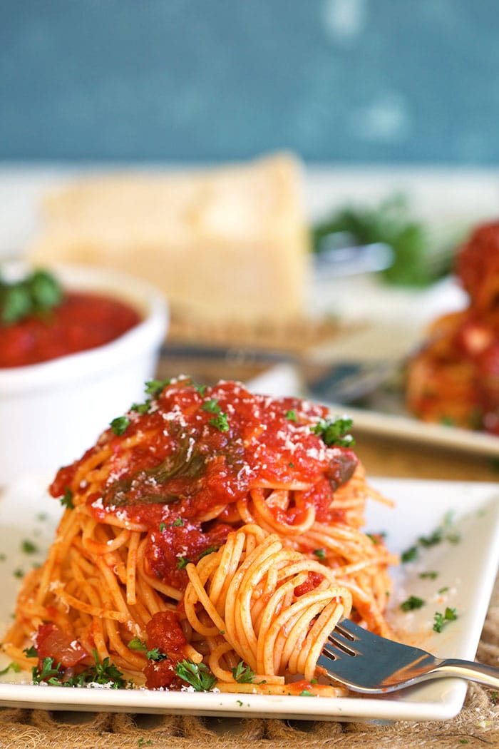 Spaghetti on a white square plate with spaghetti sauce on top and a fork with twirled pasta.