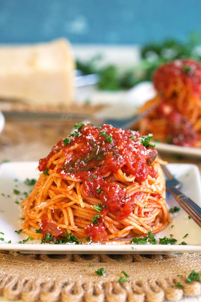 Pasta on a white square plate with homemade spaghetti sauce and a silver fork on a wicker placemat.