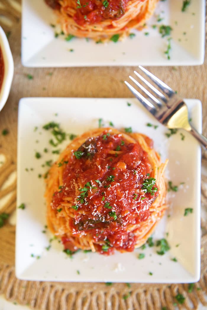 Overhead shot of spaghetti with sauce on a white square plate with a silver fork.