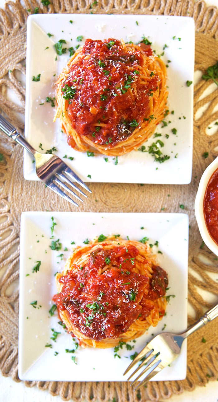 Two white square plates with spaghetti and sauce, overhead shot. 