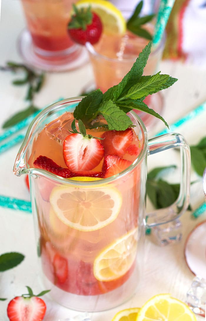 Top down view of strawberry lemonade in a clear pitcher with strawberries and lemon as a garnish.