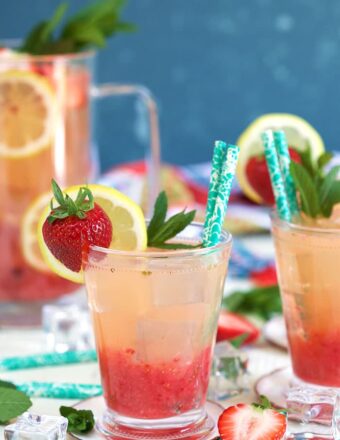 Glass of strawberry lemonade with a strawberry and lemon garnish with a turquoise colored paper straw.