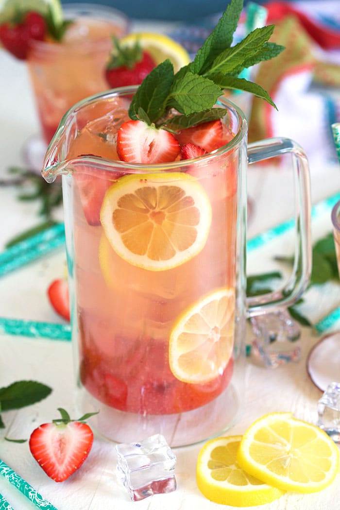 Strawberry lemonade in a glass pitcher with lemons and strawberries arranged in the pitcher as a garnish.