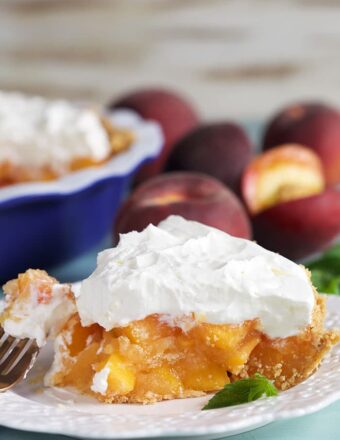 Slice of peach pie with whipped topping on a white plate.