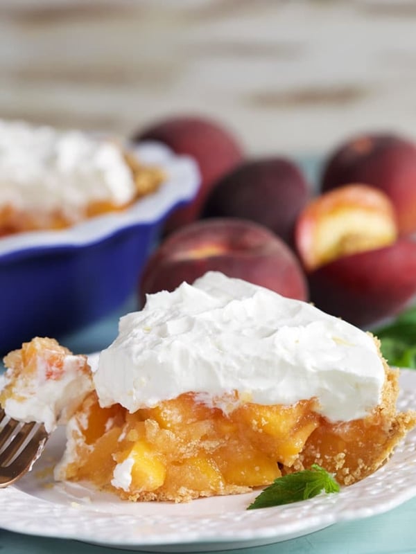 Slice of peach pie with whipped topping on a white plate.