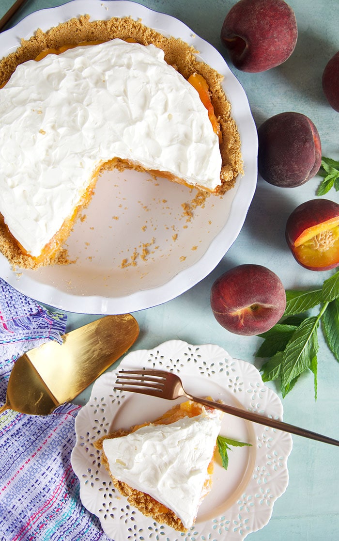 Overhead view of peach pie with whipped topping and a slice on a white plate.