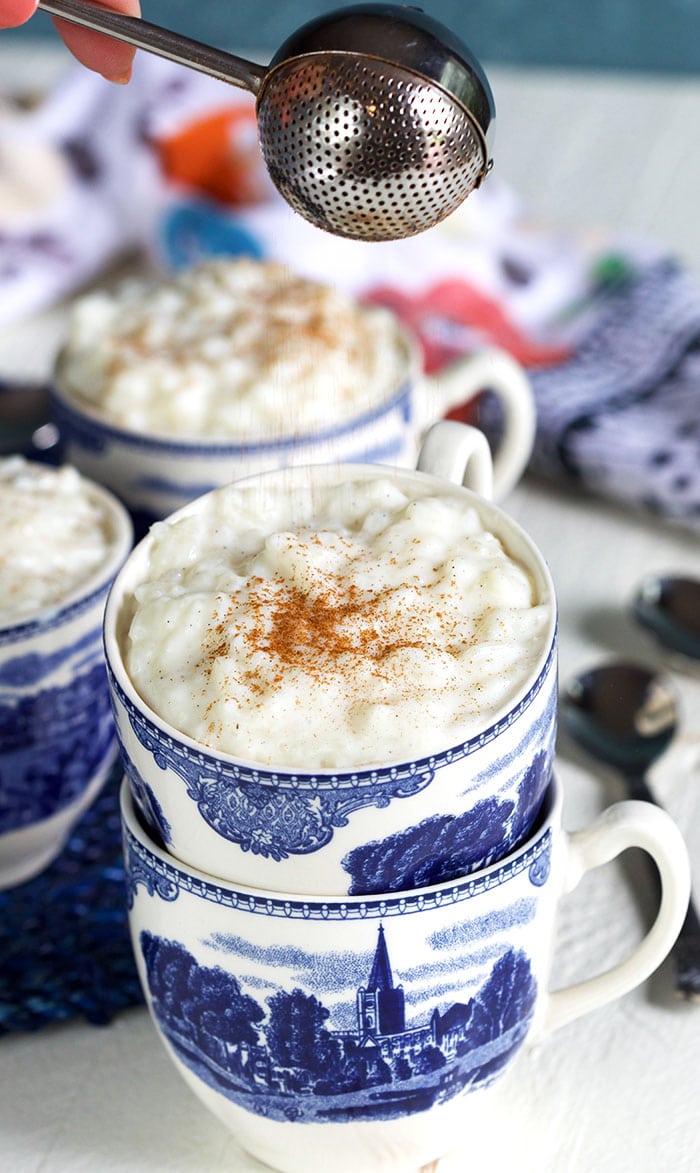 Cinnamon being sprinkled on top of rice pudding in a blue and white mug.